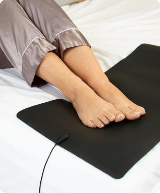 Bare feet resting on a black Earthing grounding mat on a bed