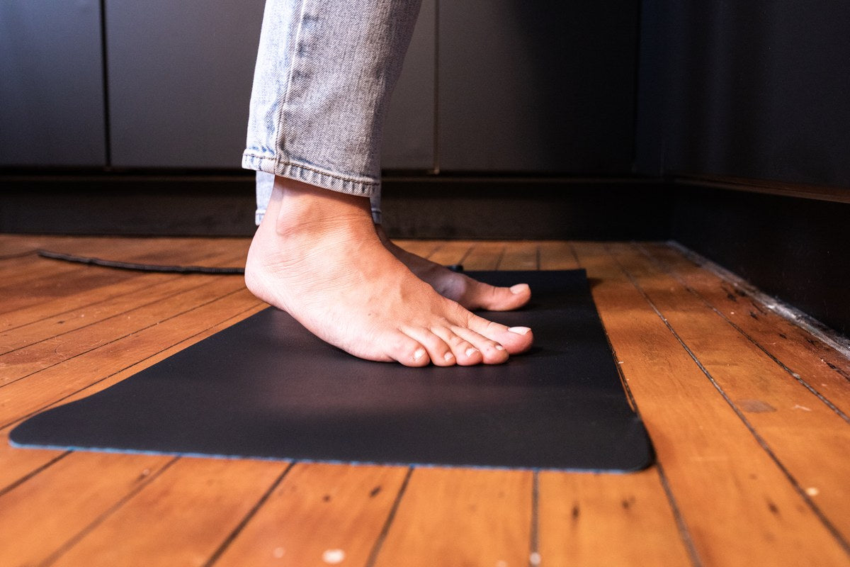 Bare feet resting on a black grounding mat on a wooden floor