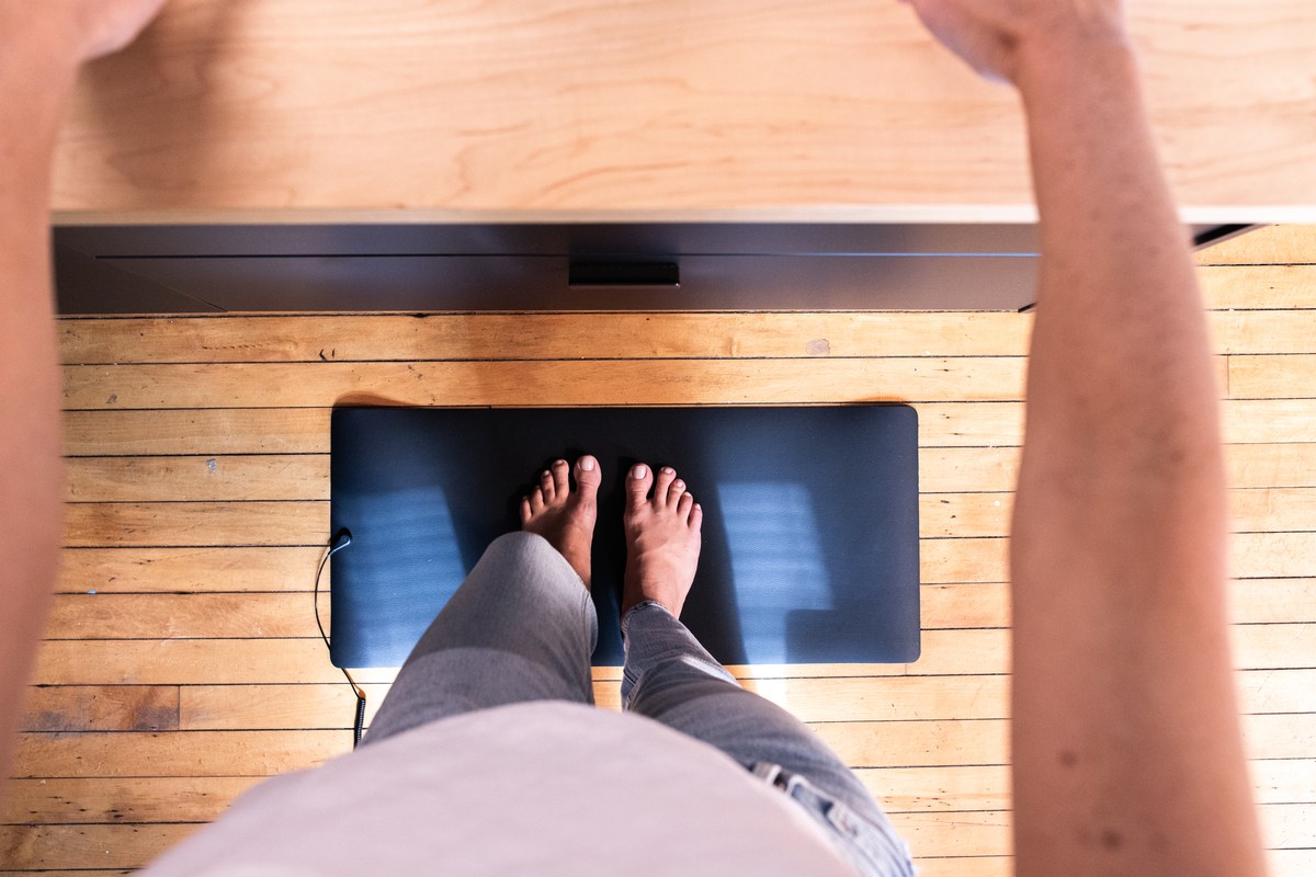 Overhead view of bare feet resting on a grounding mat beneath a home desk