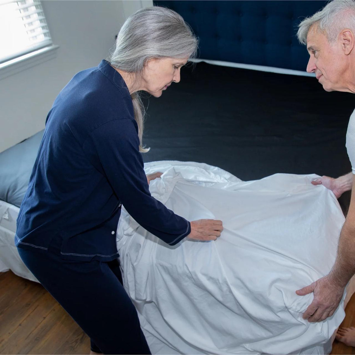 A couple fitting a white sheet over a black Earthing grounding sheet on their bed