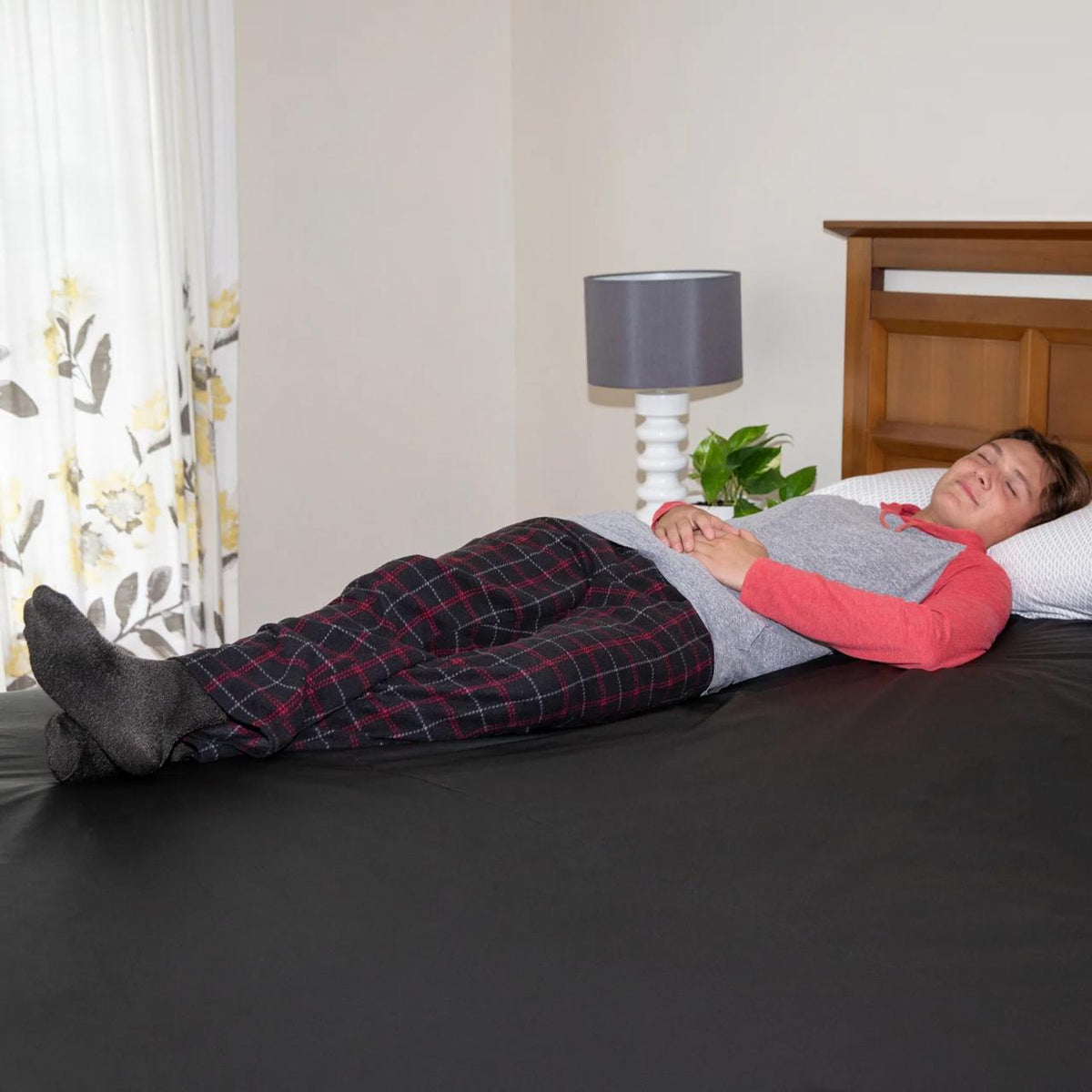 A man lying on a black Earthing grounding sheet with his eyes closed